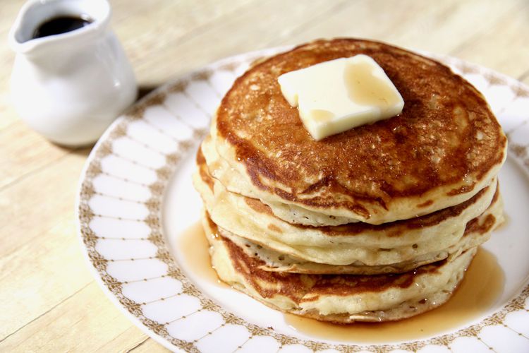 A plate with a pile of pancakes and butter on top.